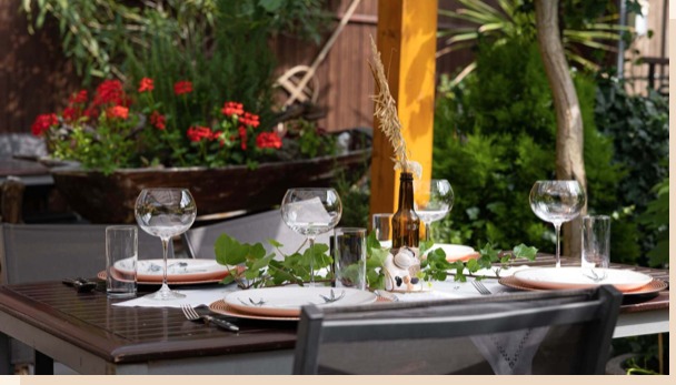 Gedeckte Gartentafel mit Efeuranken, bauchigen Gläsern und einer braunen Flasche als Vase