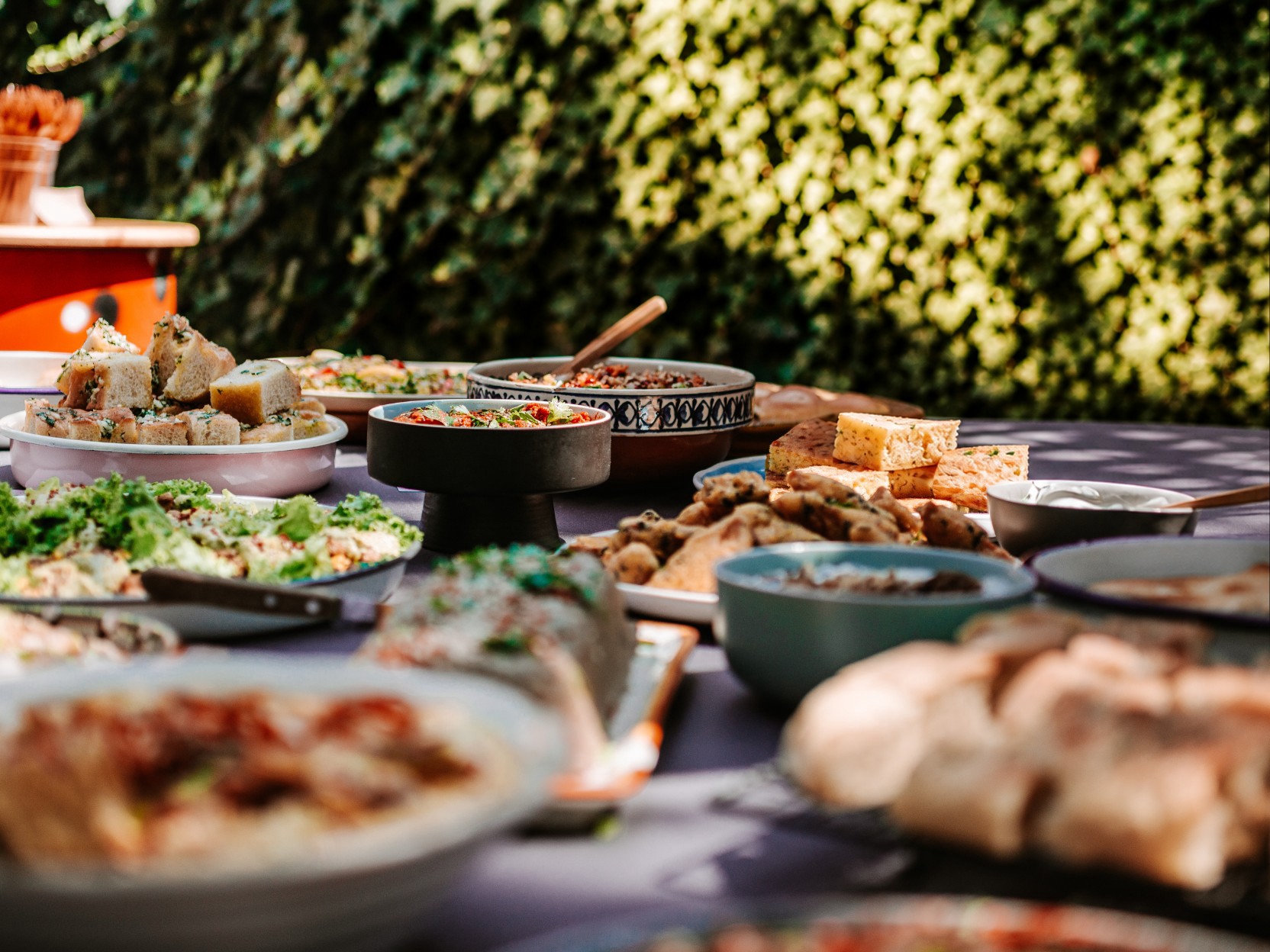Taufbuffet im Garten mit Focaccia-Würfeln, Dips, Salaten und Teigtaschen vor grüner Hecke