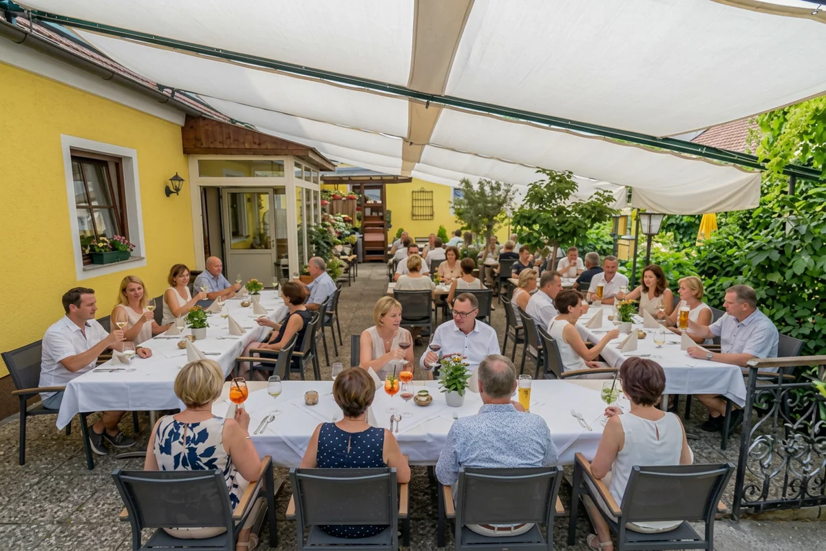 Feiernde Gäste an festlich gedeckten Tischen unter den Sonnensegeln im Garten der Bezirks Alm