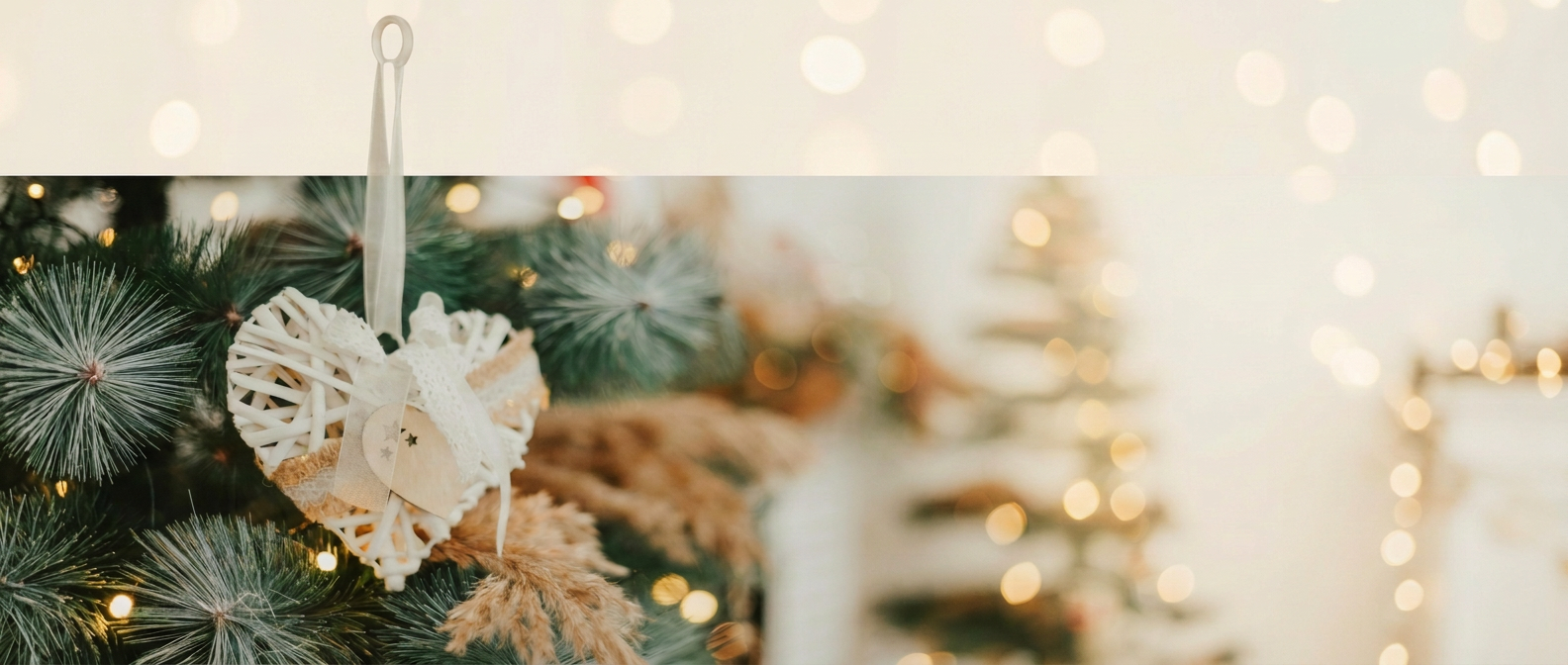 Weihnachtsdeko mit hängendem geflochtenem Holzherz, Tannenzweigen, Ziergras und Lichterkette vor weichem Lichtergrund